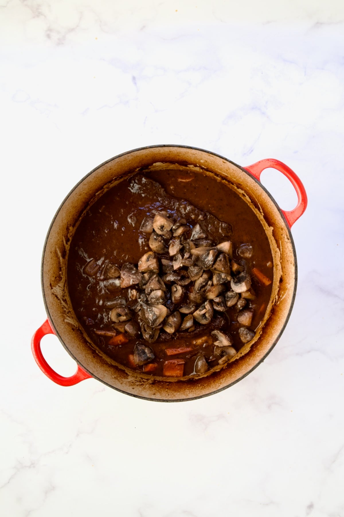 Mushrooms added to bourguignon in red Dutch oven.