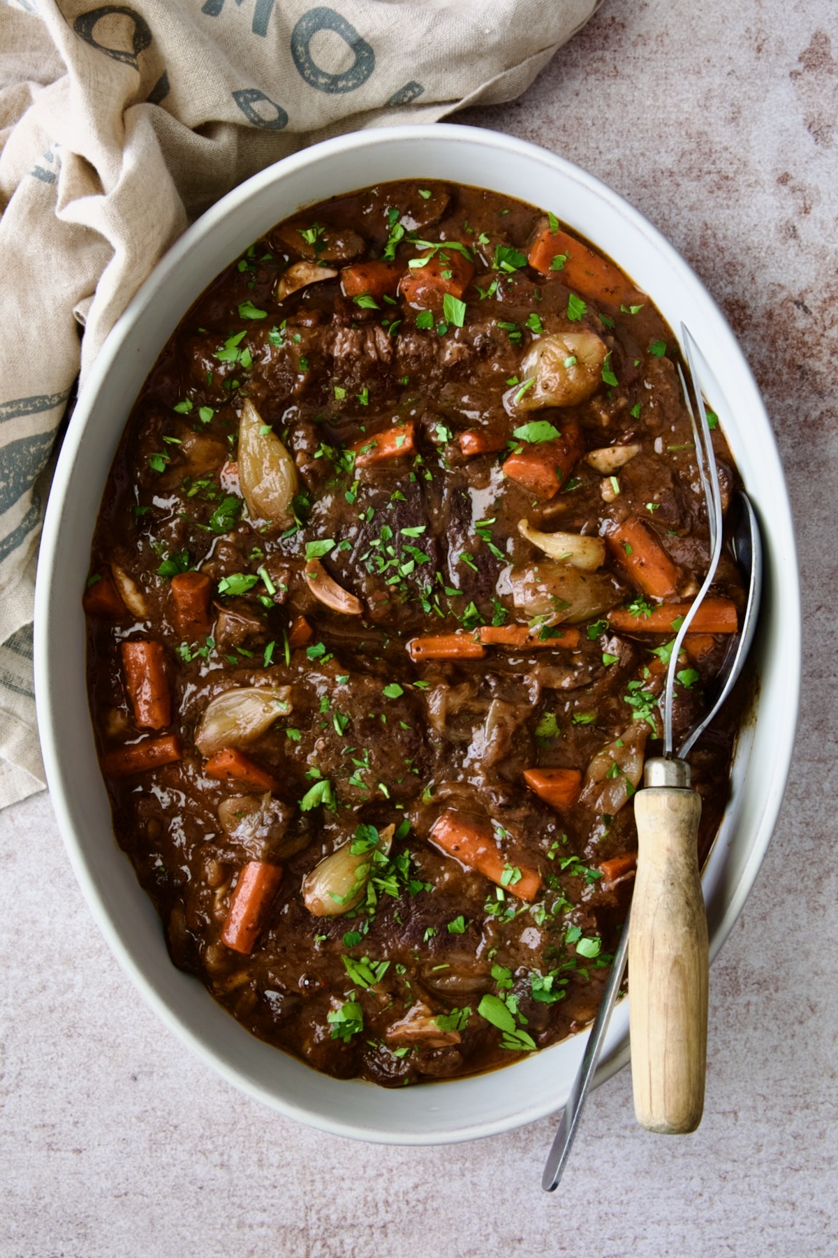 Short Ribs Bourguignon in white oval serving bowl with serving utensils.