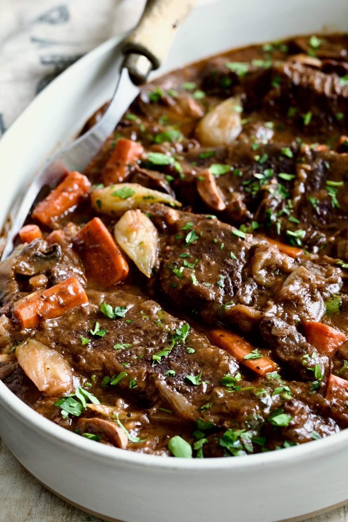 Short Ribs Bourguignon in white oval serving bowl with meat fork.