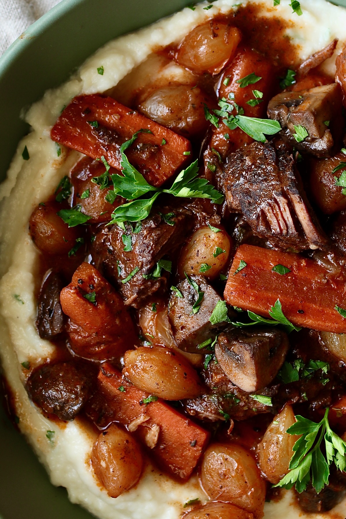 Short Ribs Bourguignon over mashed potatoes in green bowl garnished with fresh parsley.