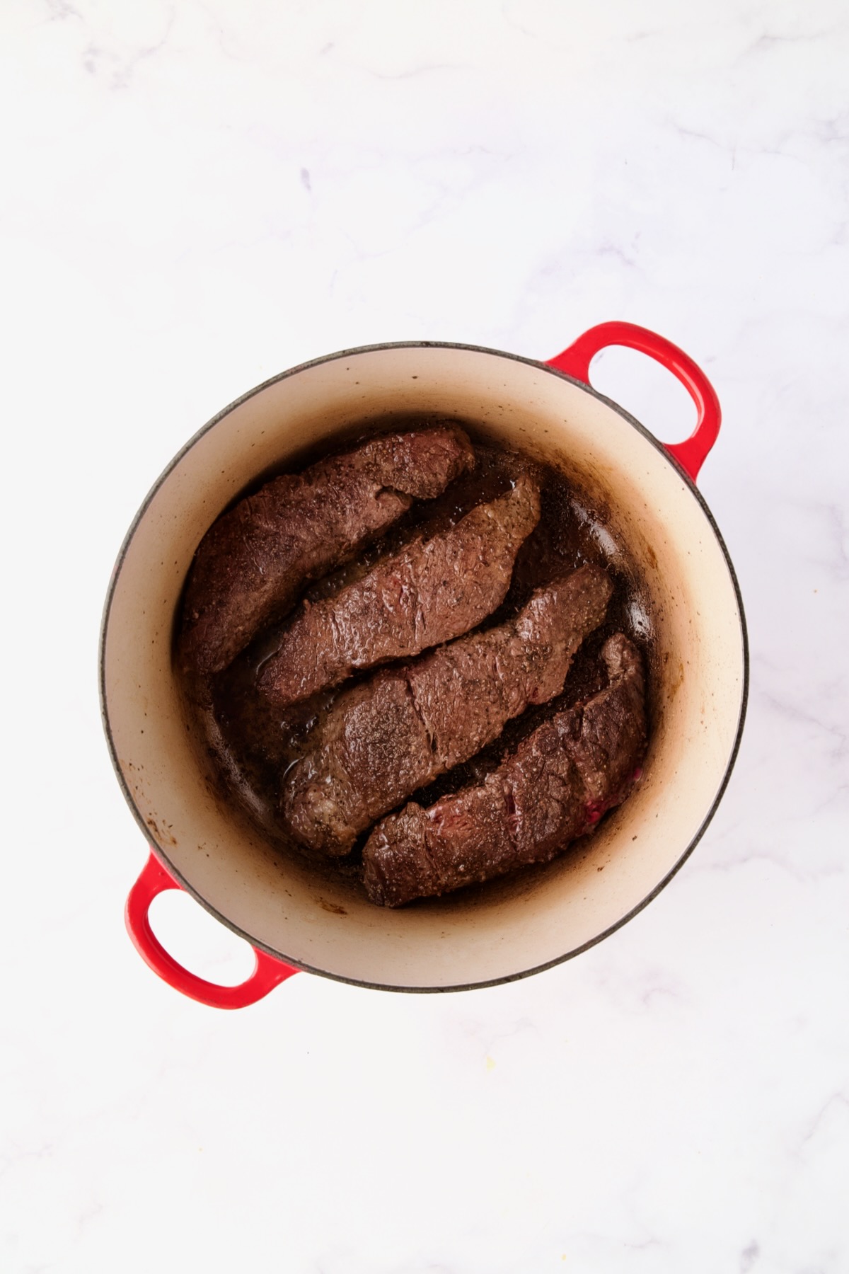 Four browned boneless beef short ribs in red Dutch oven.