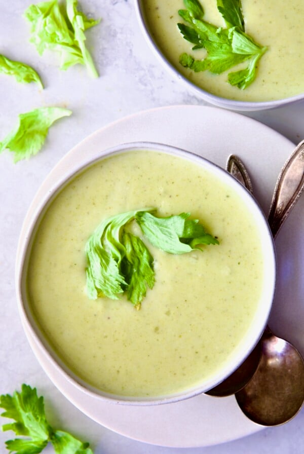 Cream of Celery Leaves Soup in white bowl on white plate with antique spoons.
