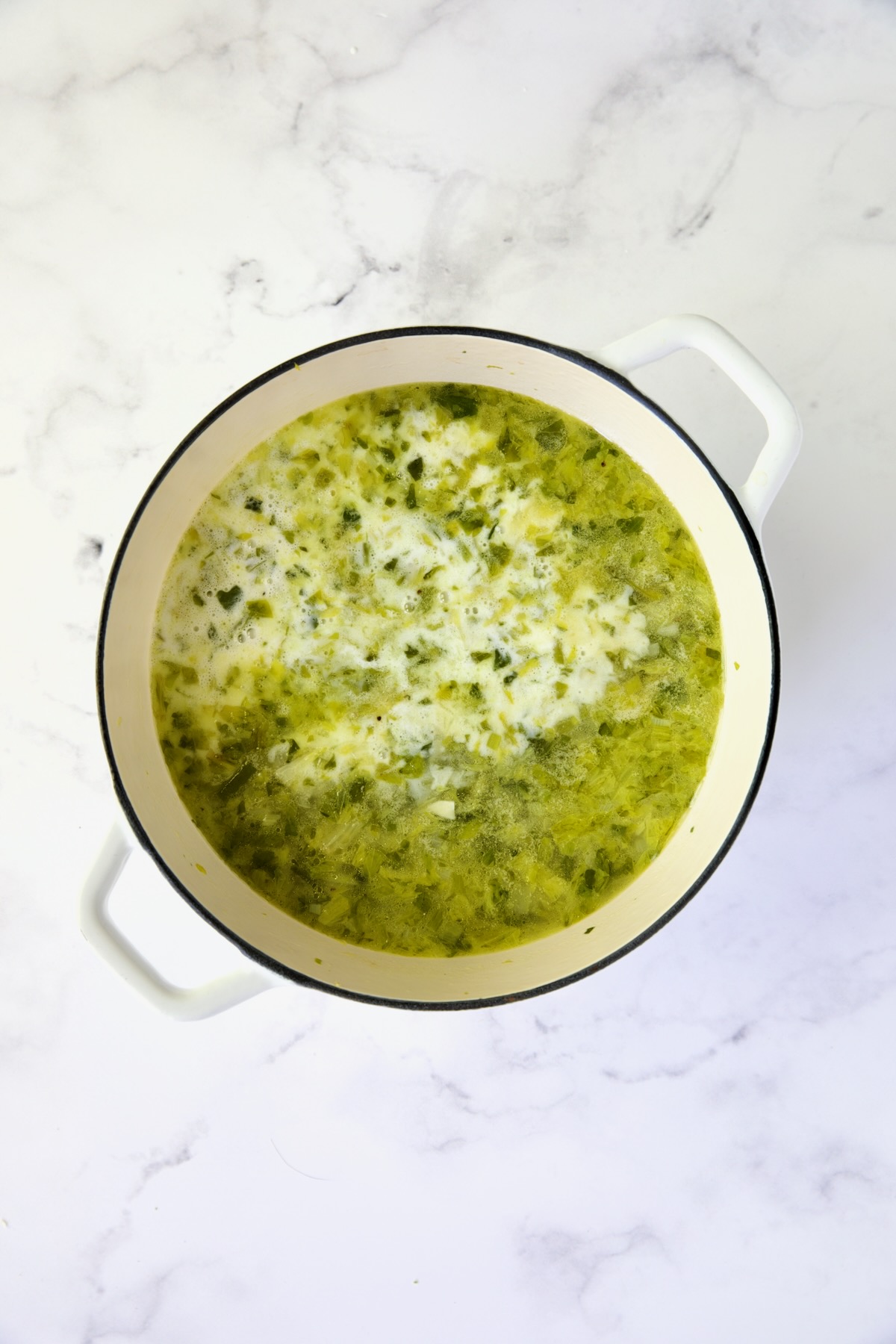 Cream added to vegetables for soup in white Dutch oven.