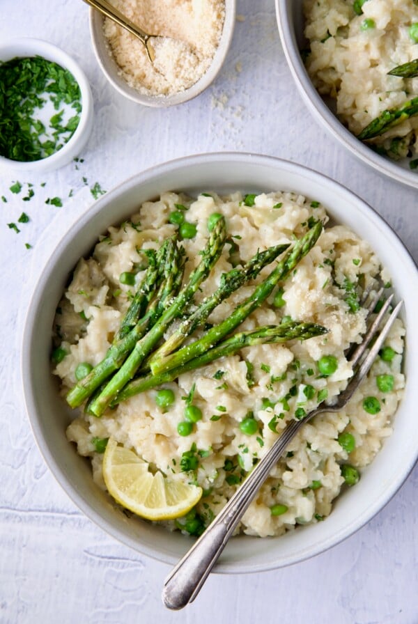 One bowl of Easy Risotto Recipe with Spring Vegetables garnished with asparagus spears and lemon wedge.