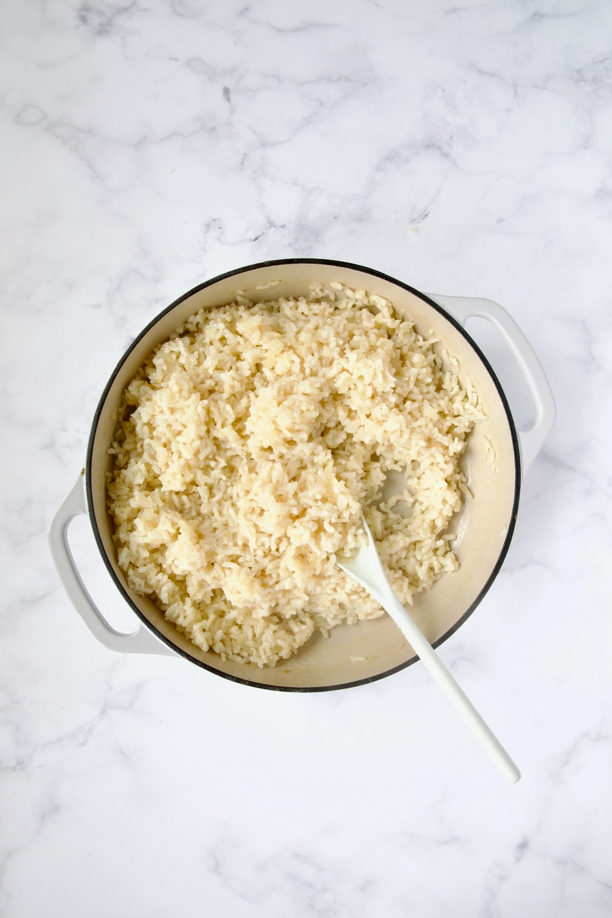 Cooked risotto in white enamel cast iron skillet.