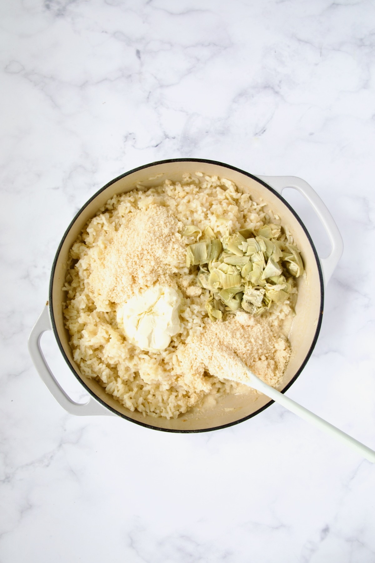 Parmesan cheese, mascarpone and artichokes added to cooked risotto in white enamel cast iron skillet.