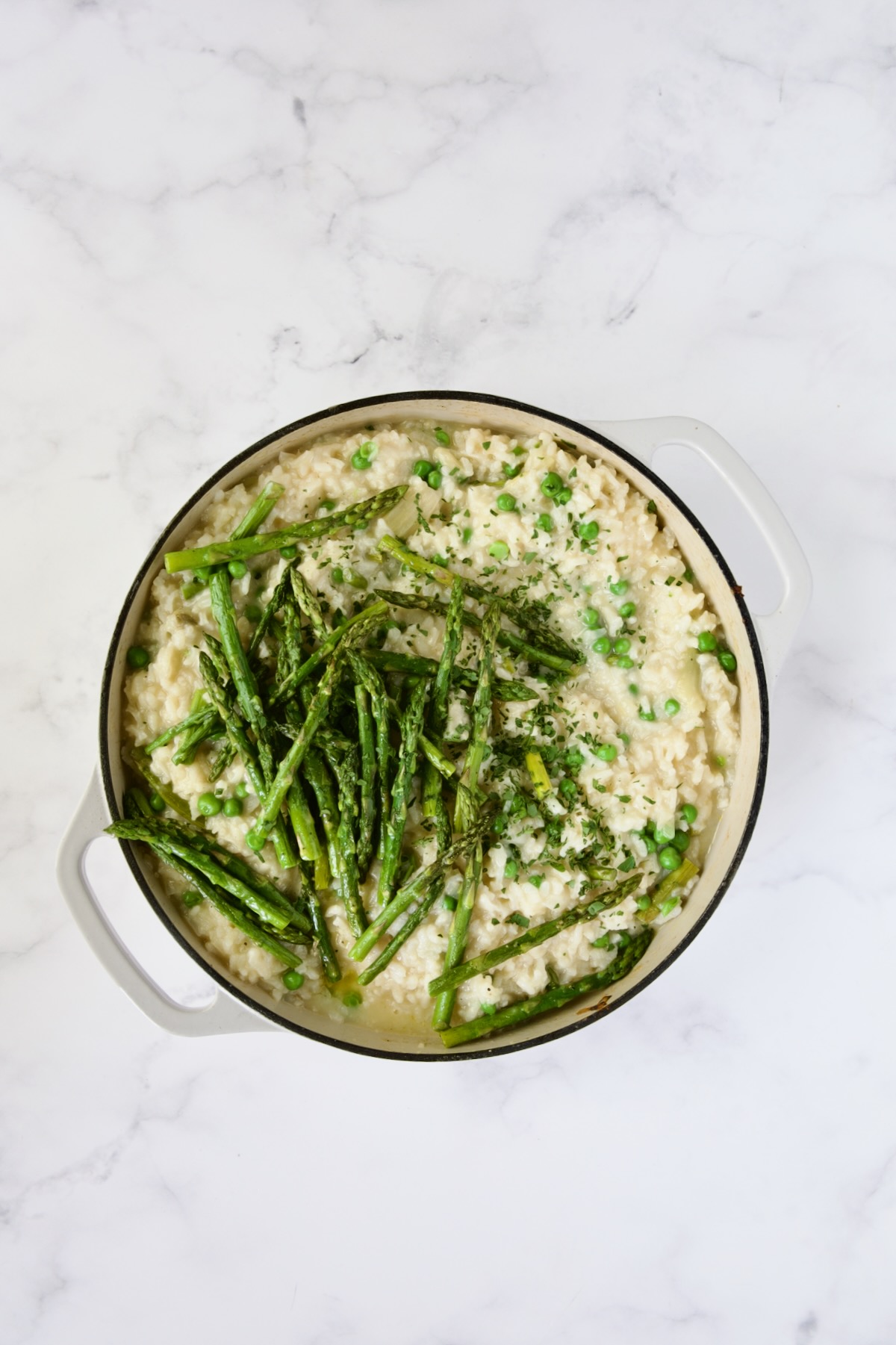 Cooked risotto topped with asparagus tips in white enamel cast iron skillet.