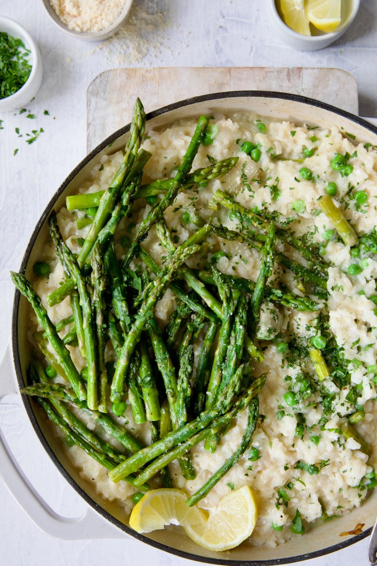 Finished risotto with asparagus tips in white enamel cast iron skillet garnished with lemon wedges.