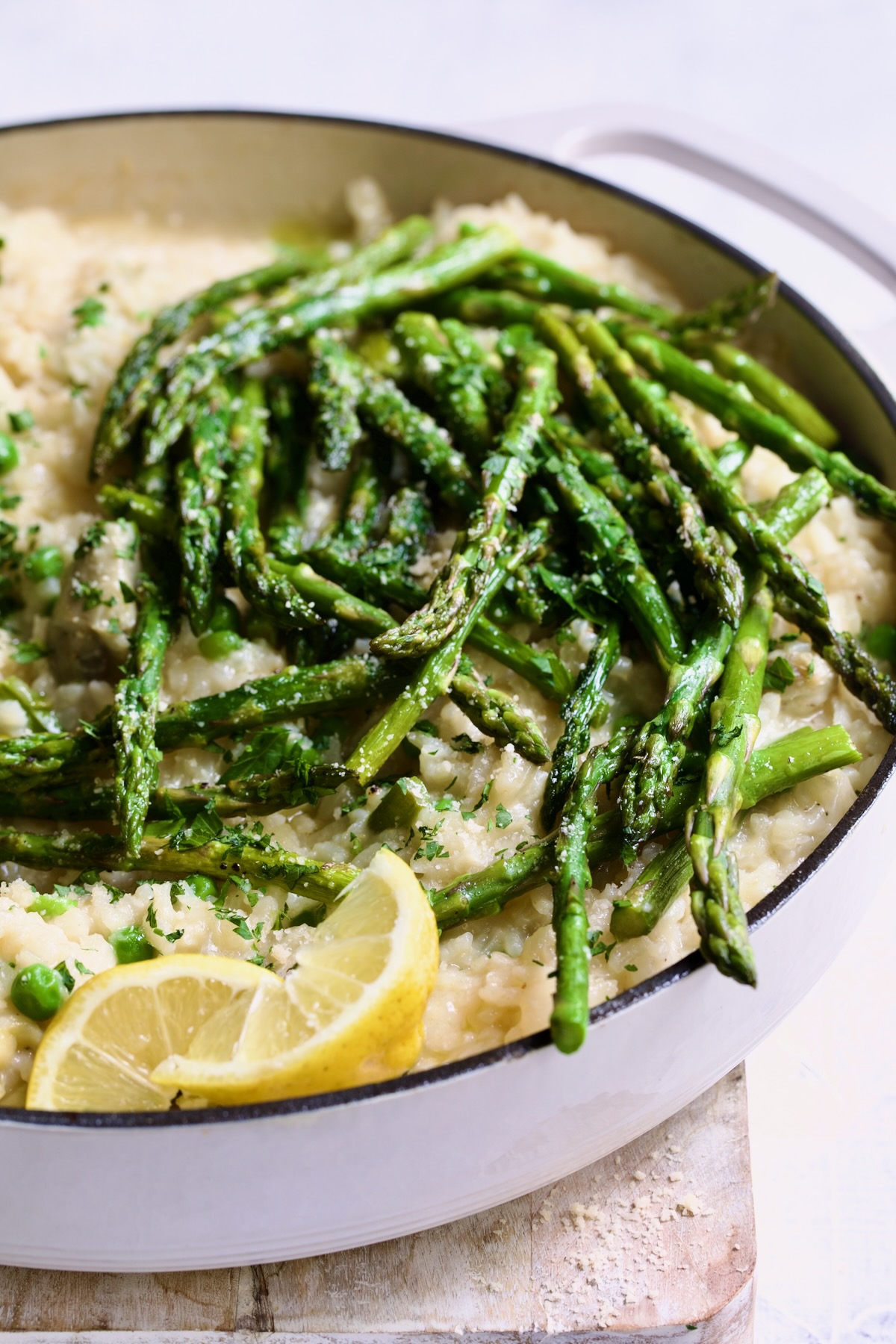 Finished risotto with asparagus tips in white enamel cast iron skillet garnished with lemon wedges.