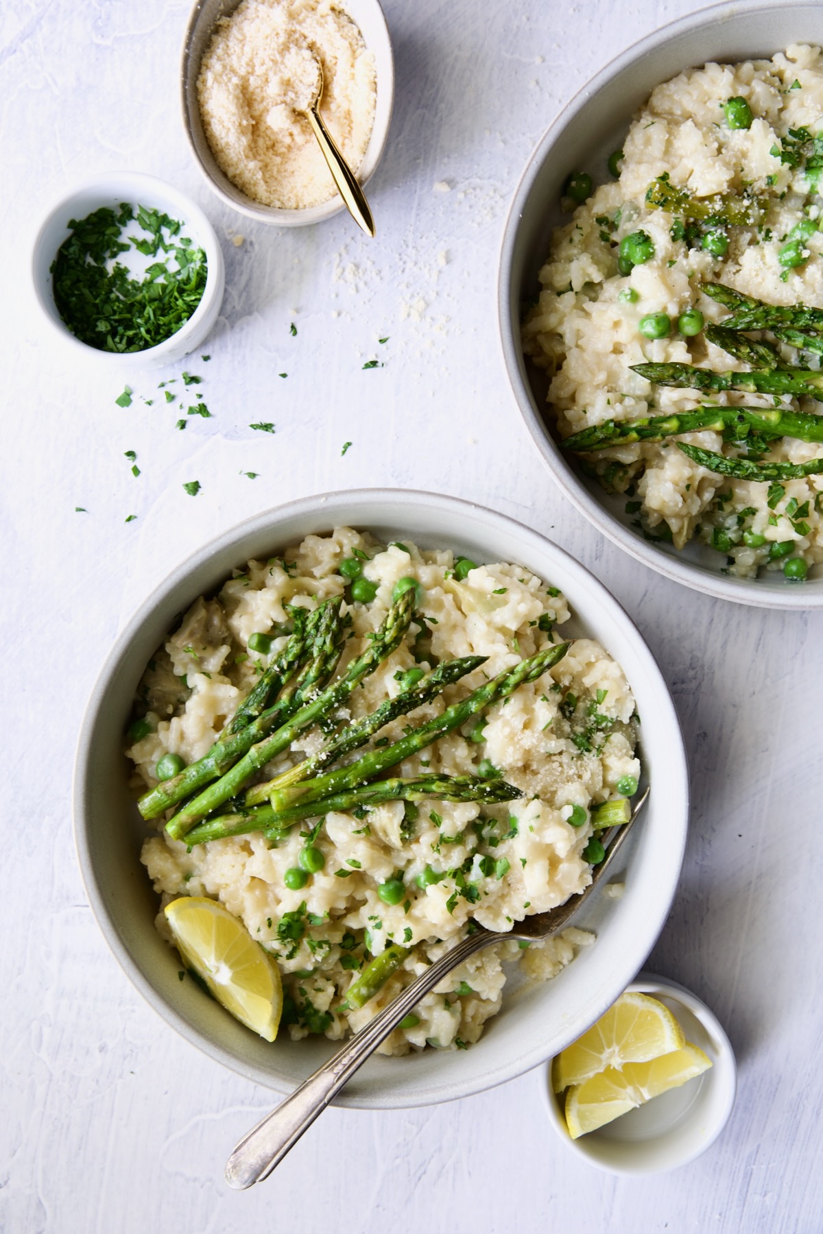 Two bowls of Easy Risotto Recipe with Spring Vegetables garnished with asparagus spears and lemon wedge.