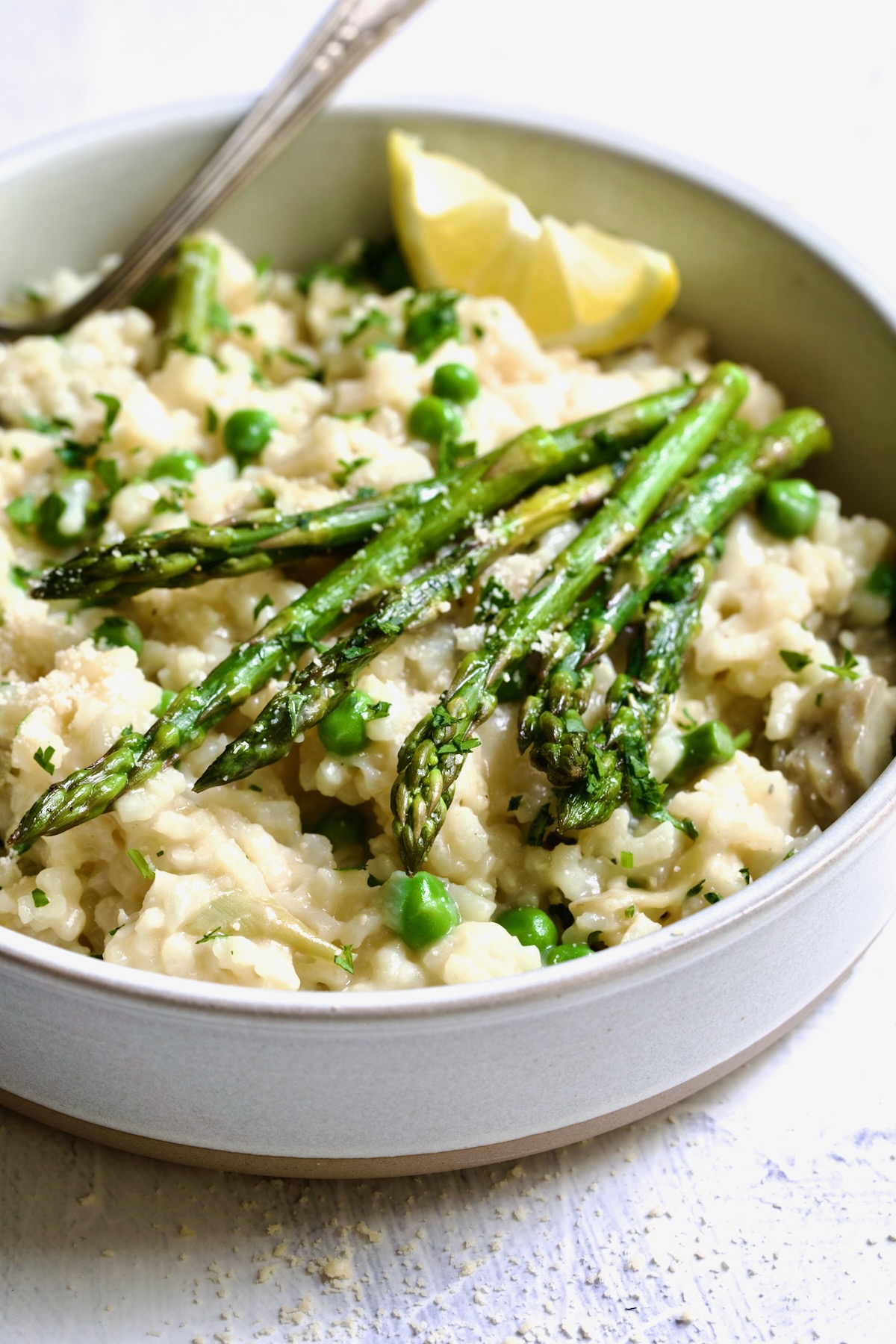 One bowl of Easy Risotto Recipe with Spring Vegetables with asparagus spears on the top and lemon wedge.