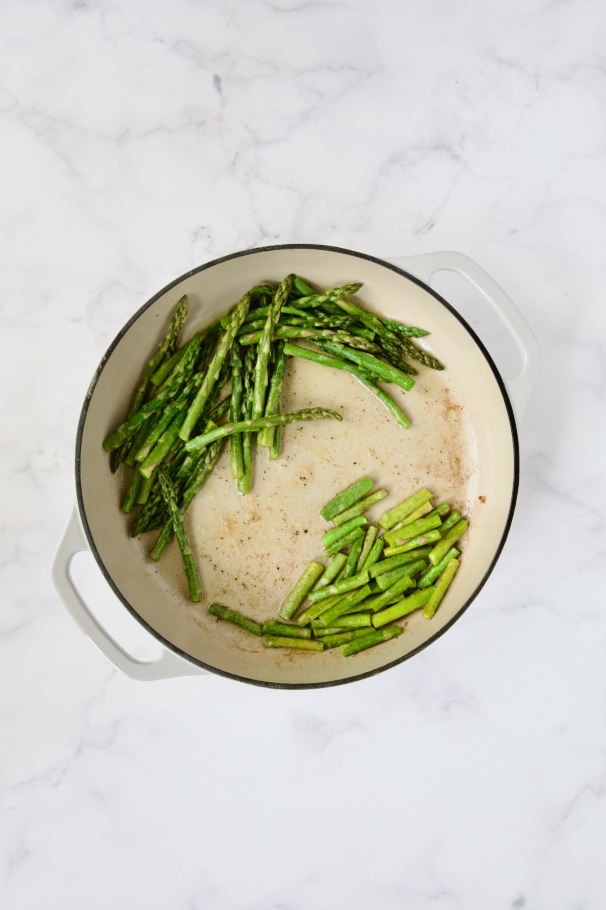 Asparagus tips and stems in white enamel cast iron skillet.