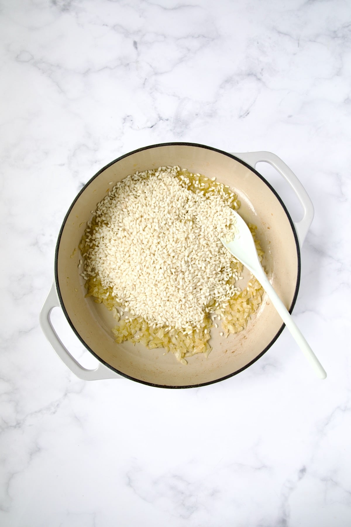 Arborio rice added to onions and garlic in white enamel cast iron skillet.