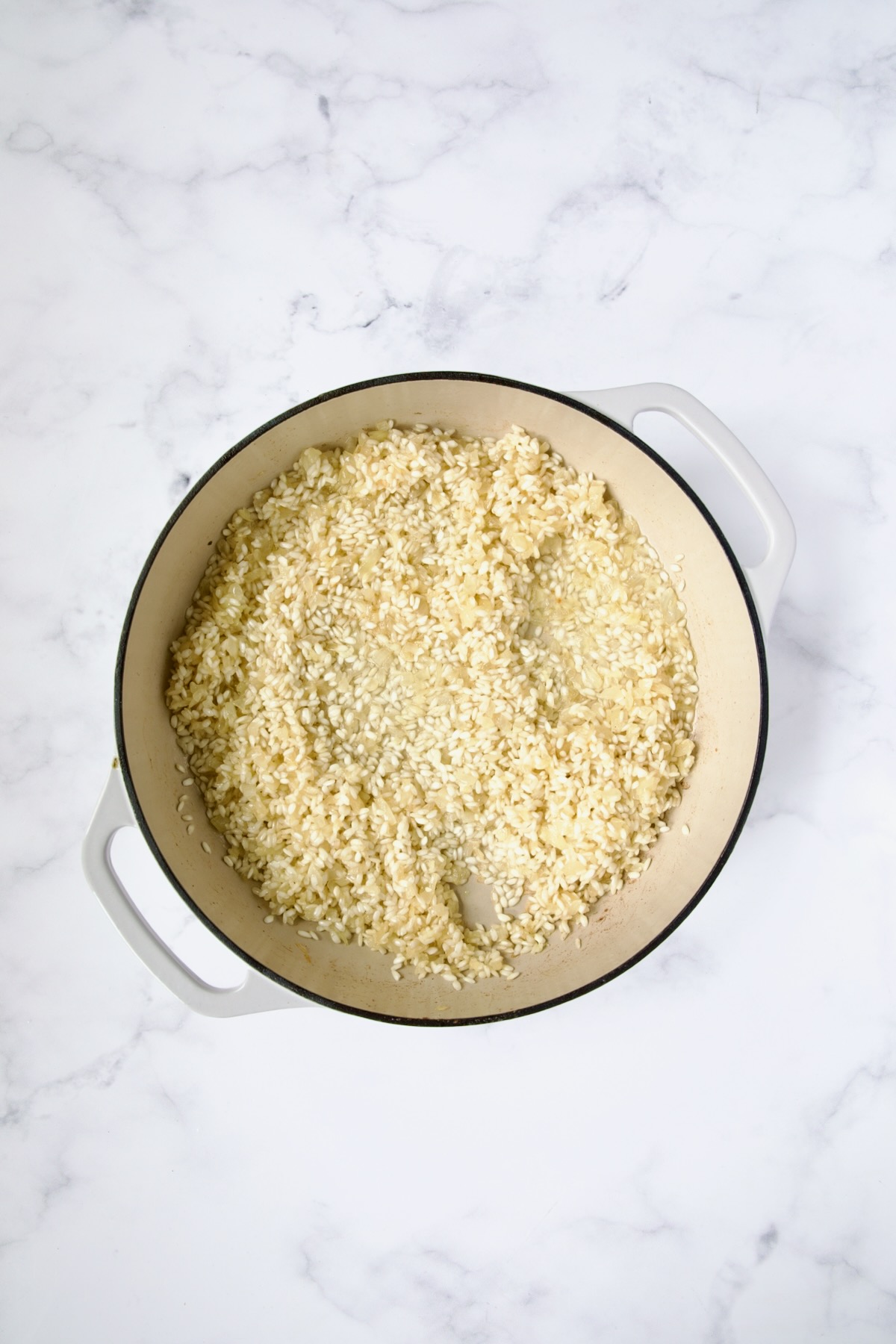 Wine added to rice, onions and garlic in white enamel cast iron skillet.
