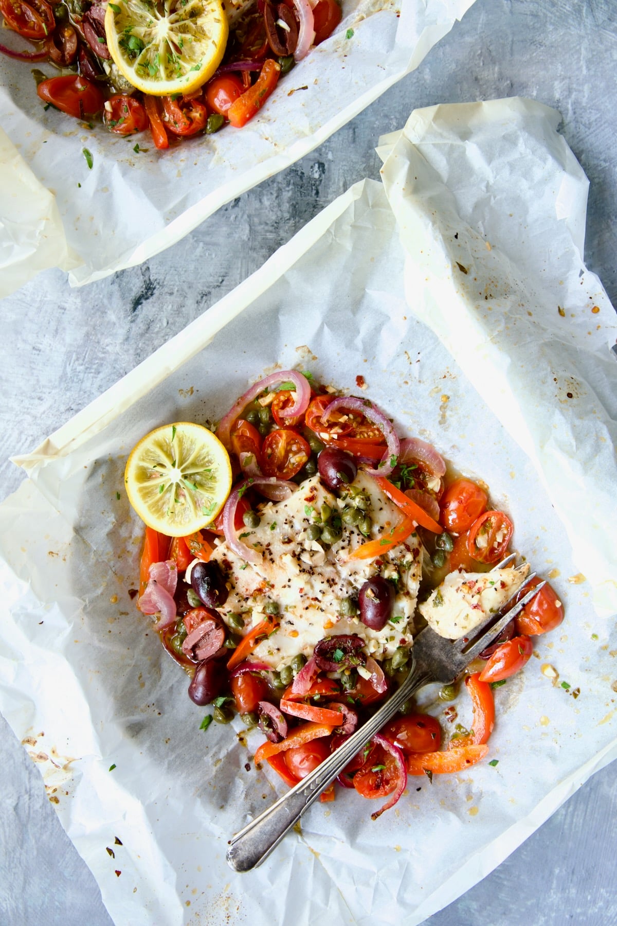Baked Mediterranean Fish en Papillote on parchment paper with a piece on antique fork.