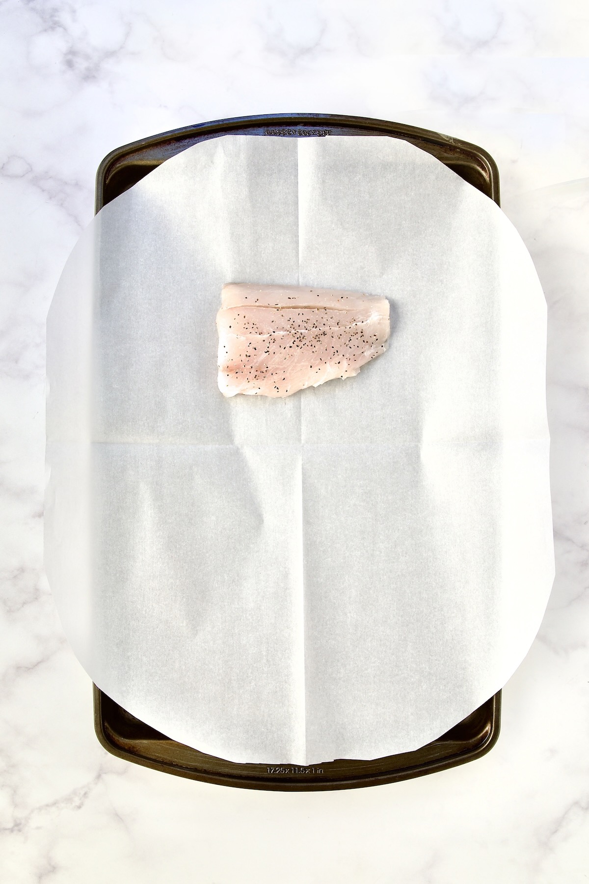 Piece of fish on parchment paper on rimmed sheet pan.