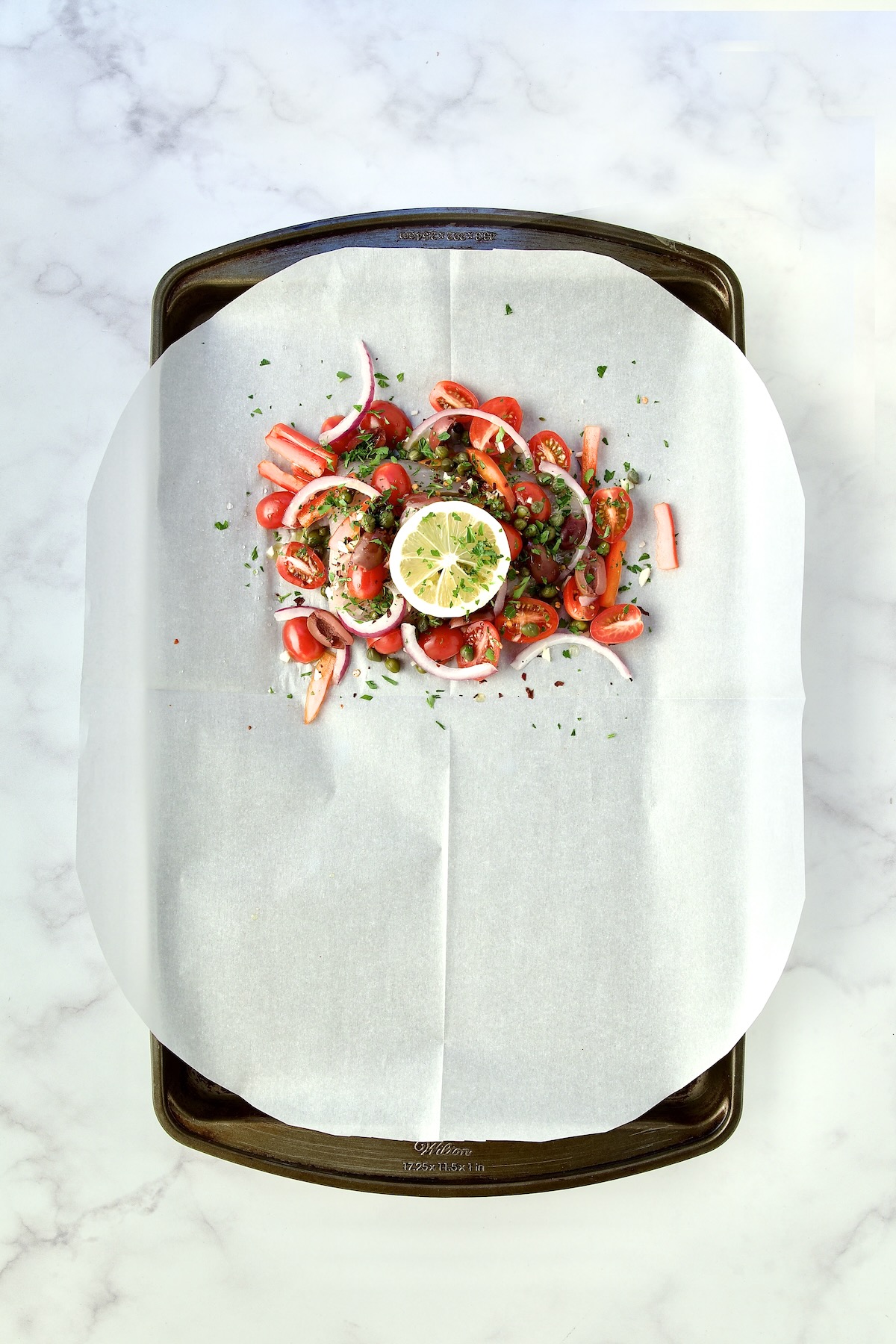 Assembled fish and other ingredients on parchment paper on rimmed sheet pan.