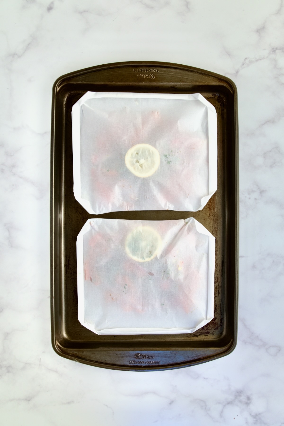 Folded parchment paper packets on rimmed sheet pan ready to be baked.