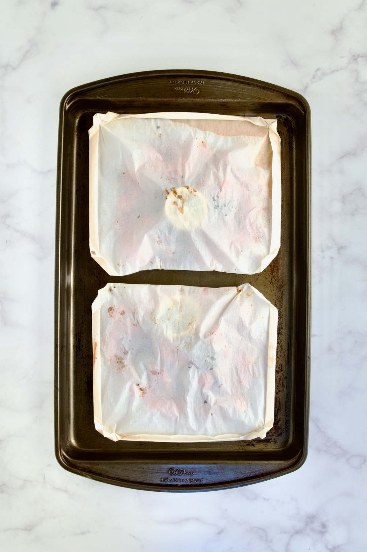 Two baked parchment paper packages on rimmed sheet pan.