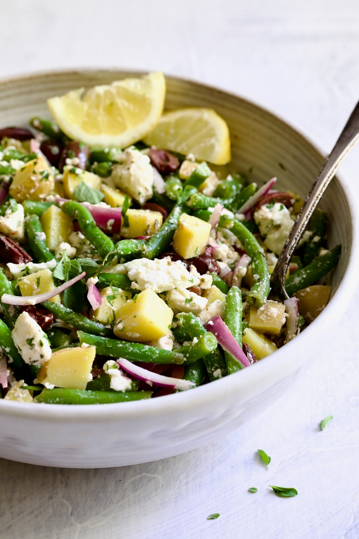 Potato Green Bean Salad in white bowl with serving spoon.