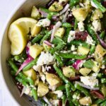 Potato Green Bean Salad in white bowl with lemon wedges.