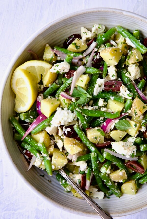Potato Green Bean Salad in white bowl with lemon wedges.