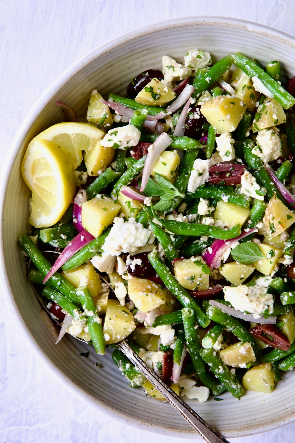 Potato Green Bean Salad in white bowl with lemon wedges.