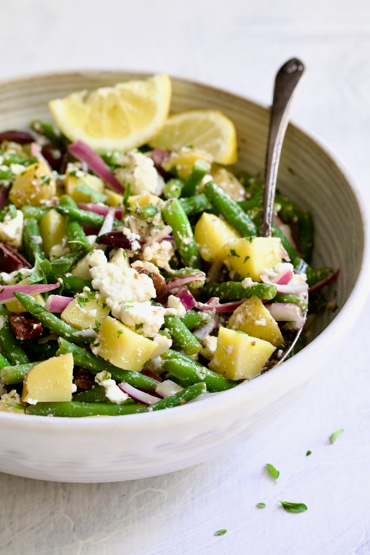 Potato Green Bean Salad in white bowl with serving spoon.