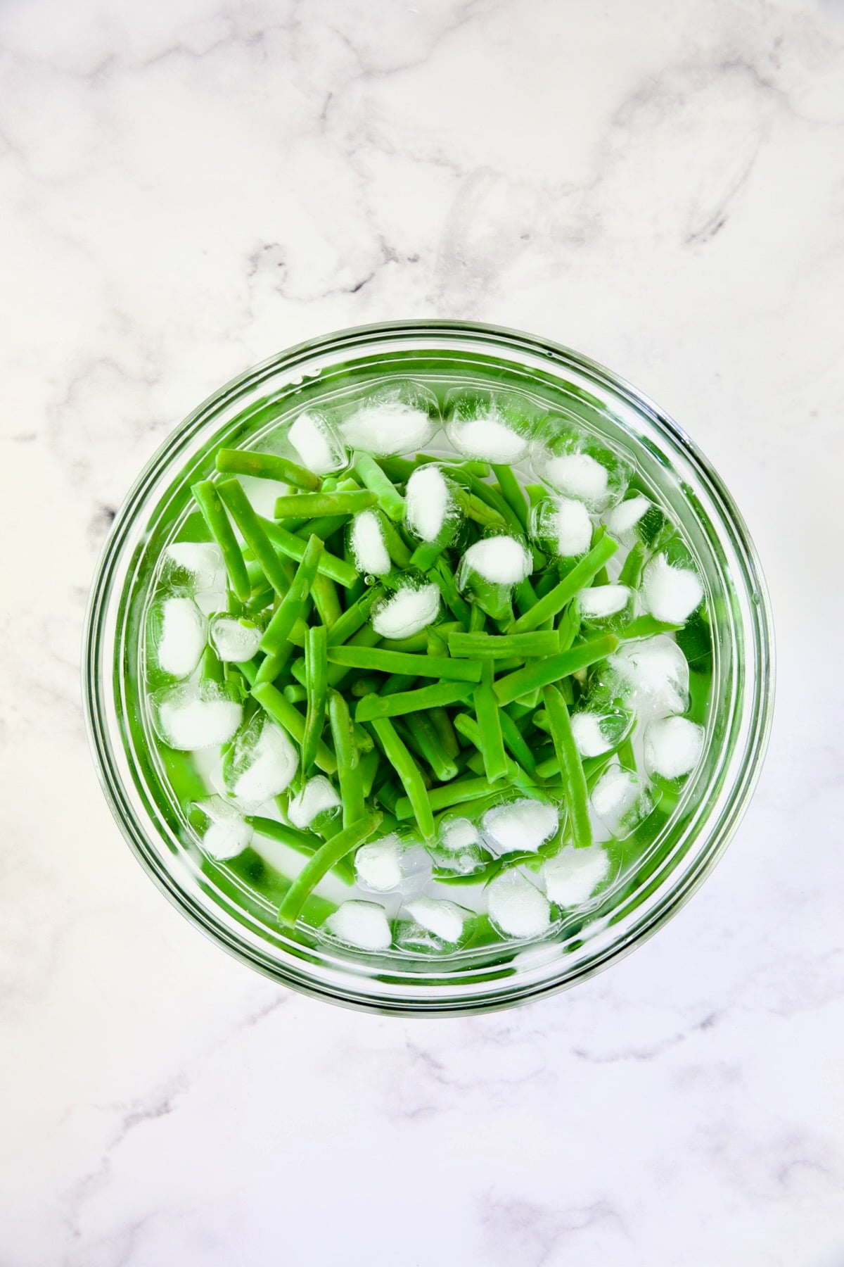 Green beans in ice bath in glass bowl.