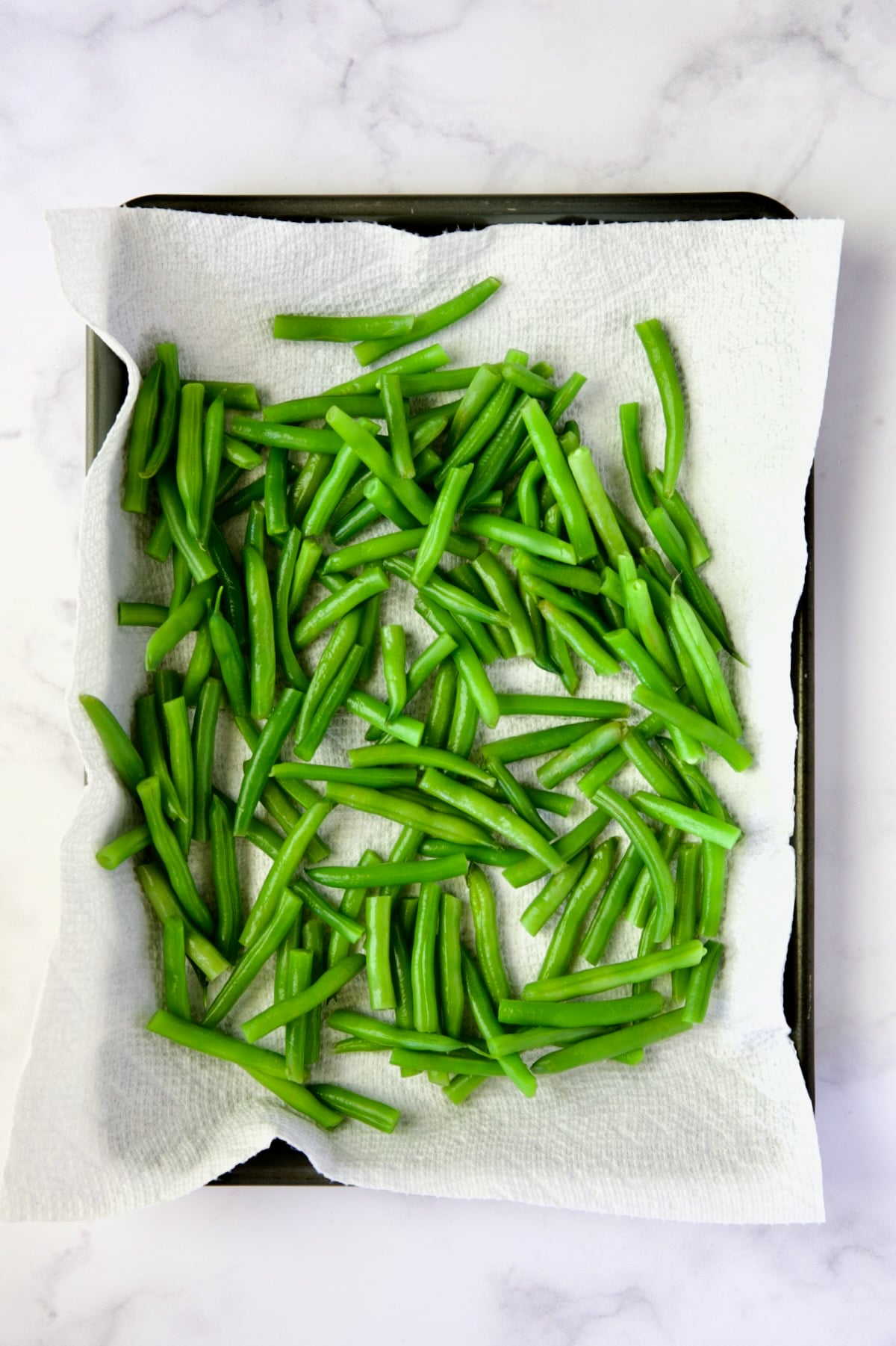 Blanched green beans on paper towel-lined rimmed baking sheet.