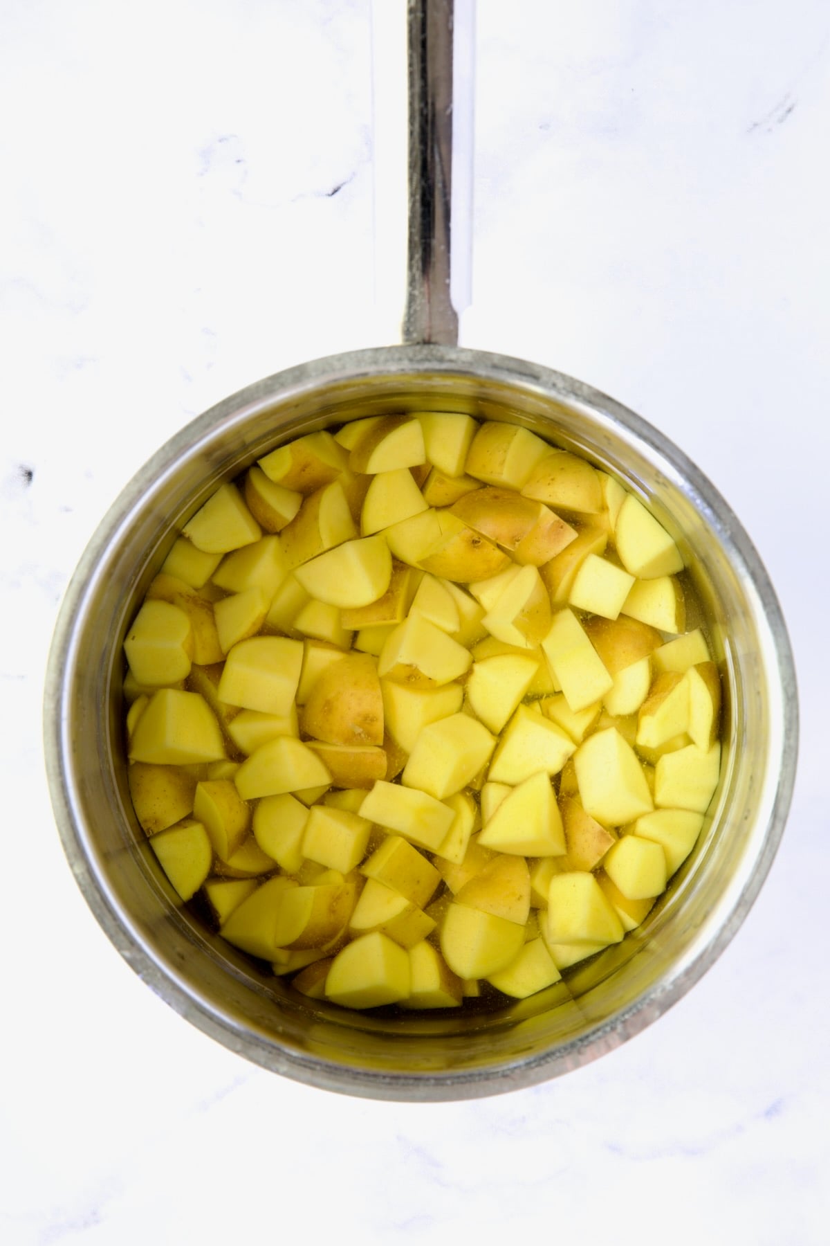 Cubed Yukon Gold potatoes in water in stainless steel saucepan.