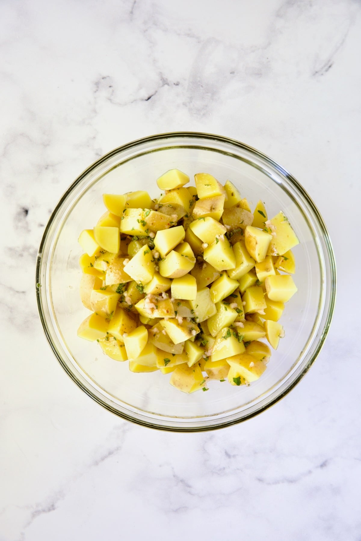 Cooked Yukon Gold potatoes with vinaigrette in glass bowl.