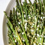 Roasted Asparagus with Walnut Lemon Gremolata and Goat Cheese on white oval platter with lemon wedges.