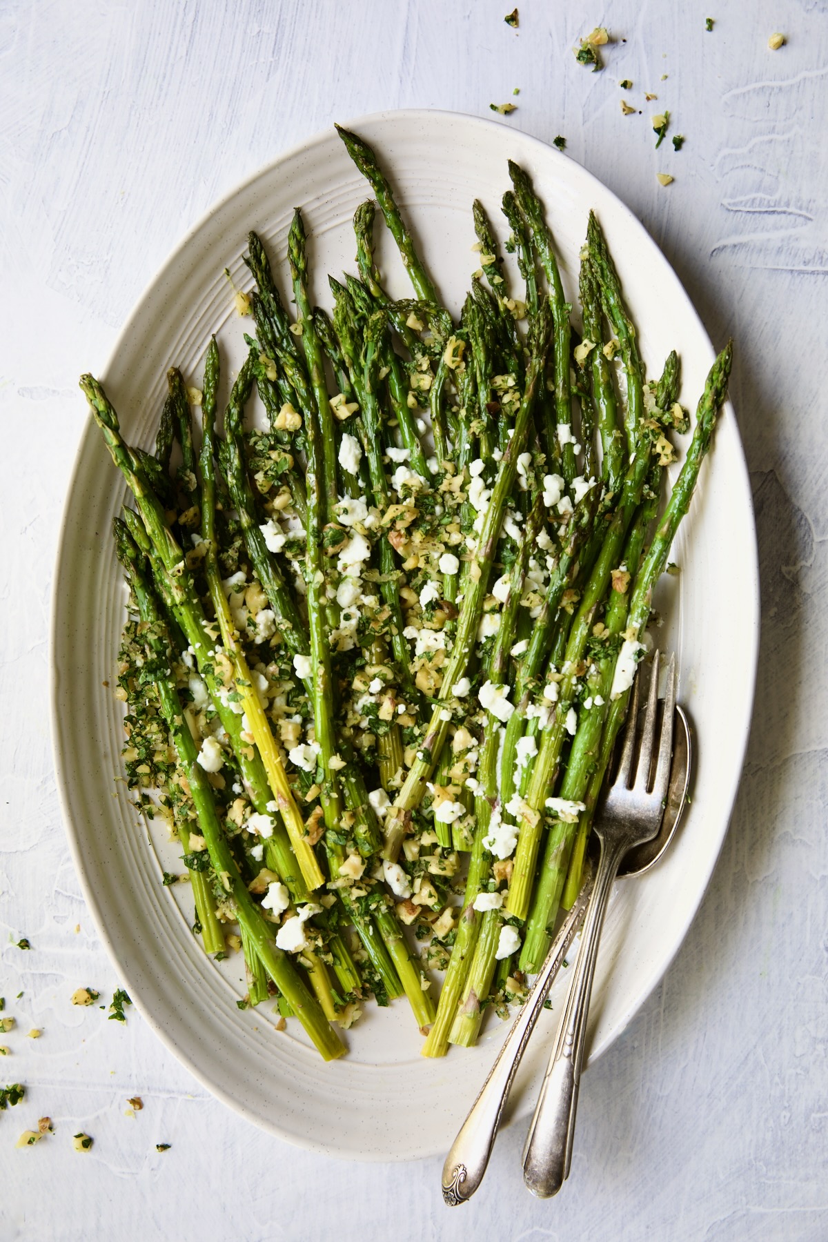 Roasted Asparagus with Walnut Lemon Gremolata and Goat Cheese on white oval platter.