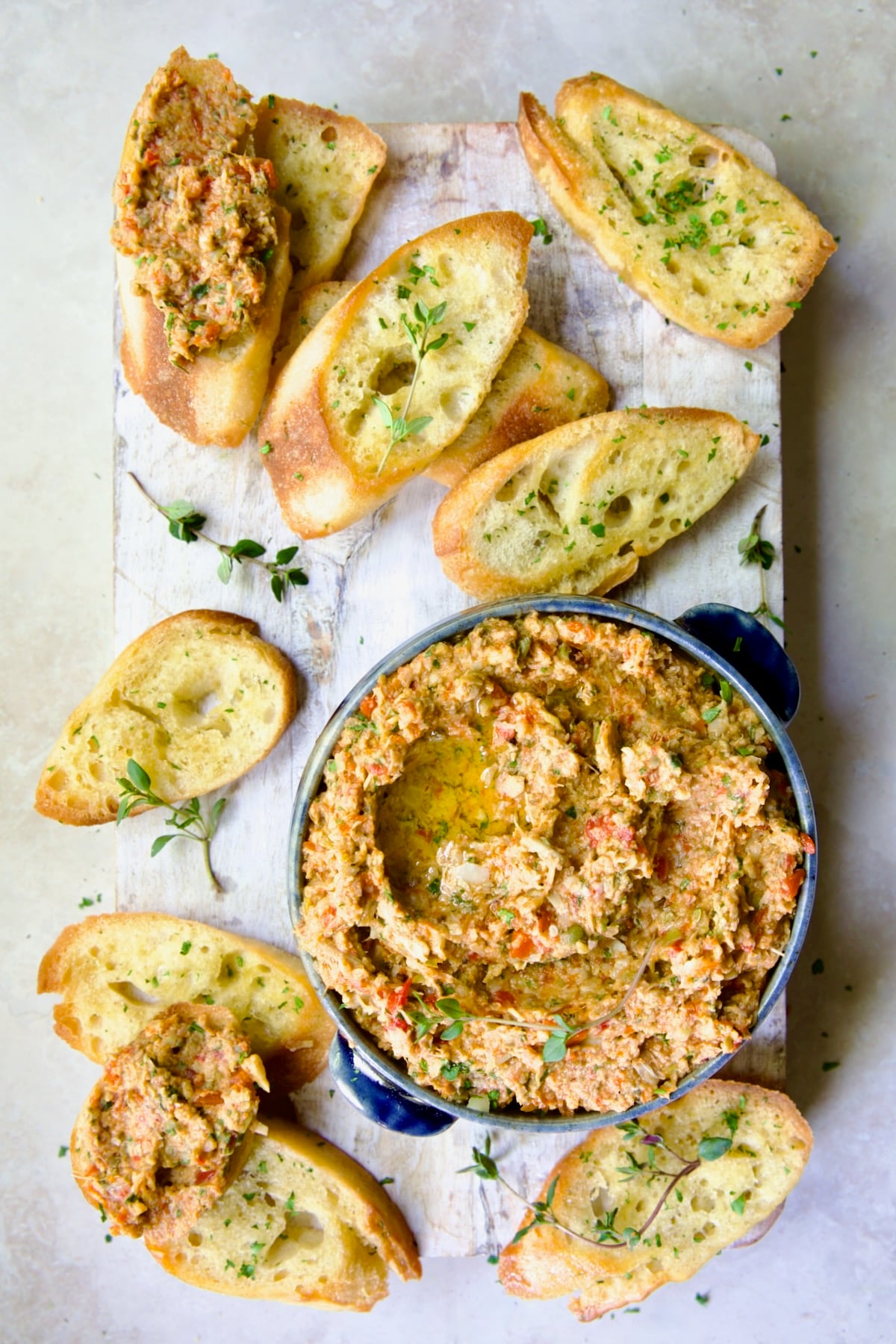 Artichoke Tapenade with Crostini on whitewashed board garnished with fresh thyme.