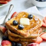 Brioche French Toast on white plate with pat of butter, blueberries and strawberries.