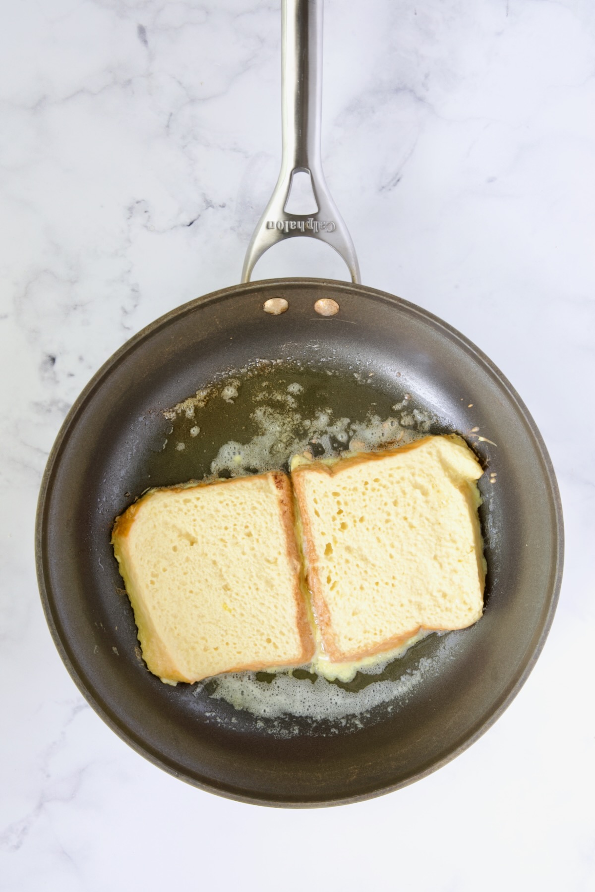 Two slices of french toast in nonstick skillet being cooked on the first side.