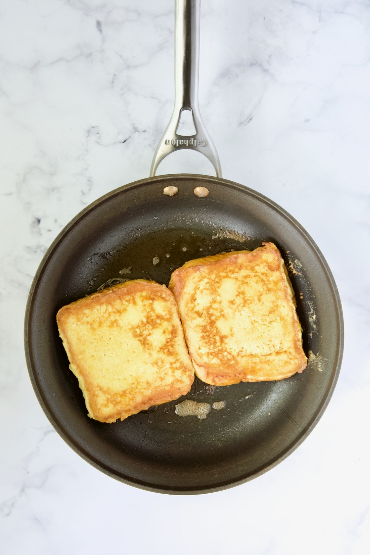 Two slices of french toast in nonstick skillet being cooked after being flipped to cook on the other side.
