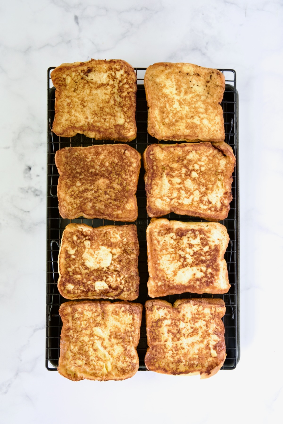 Eight slices of fully cooked french toast on cooling rack set over rimmed sheet pan.