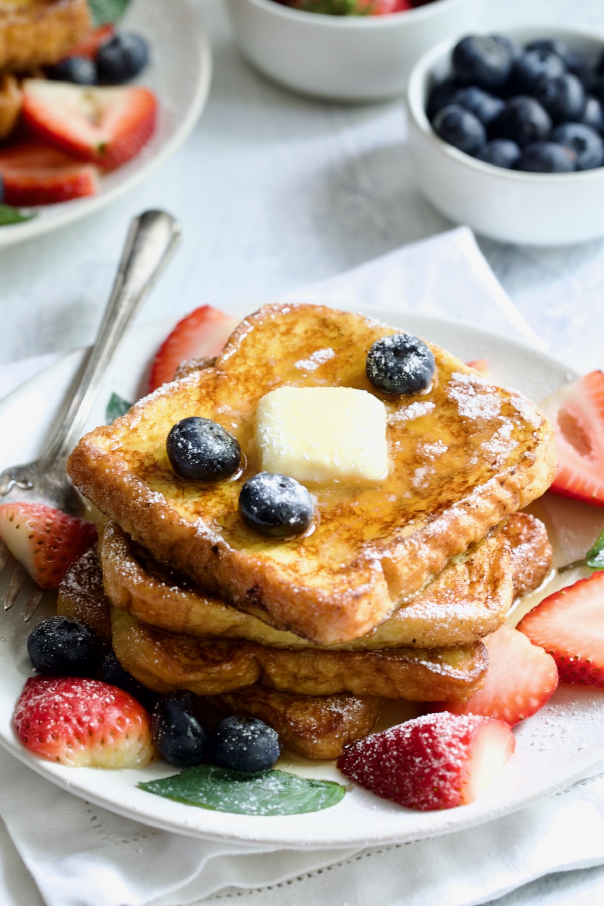 Brioche French Toast on white plate with pat of butter, blueberries and strawberries.