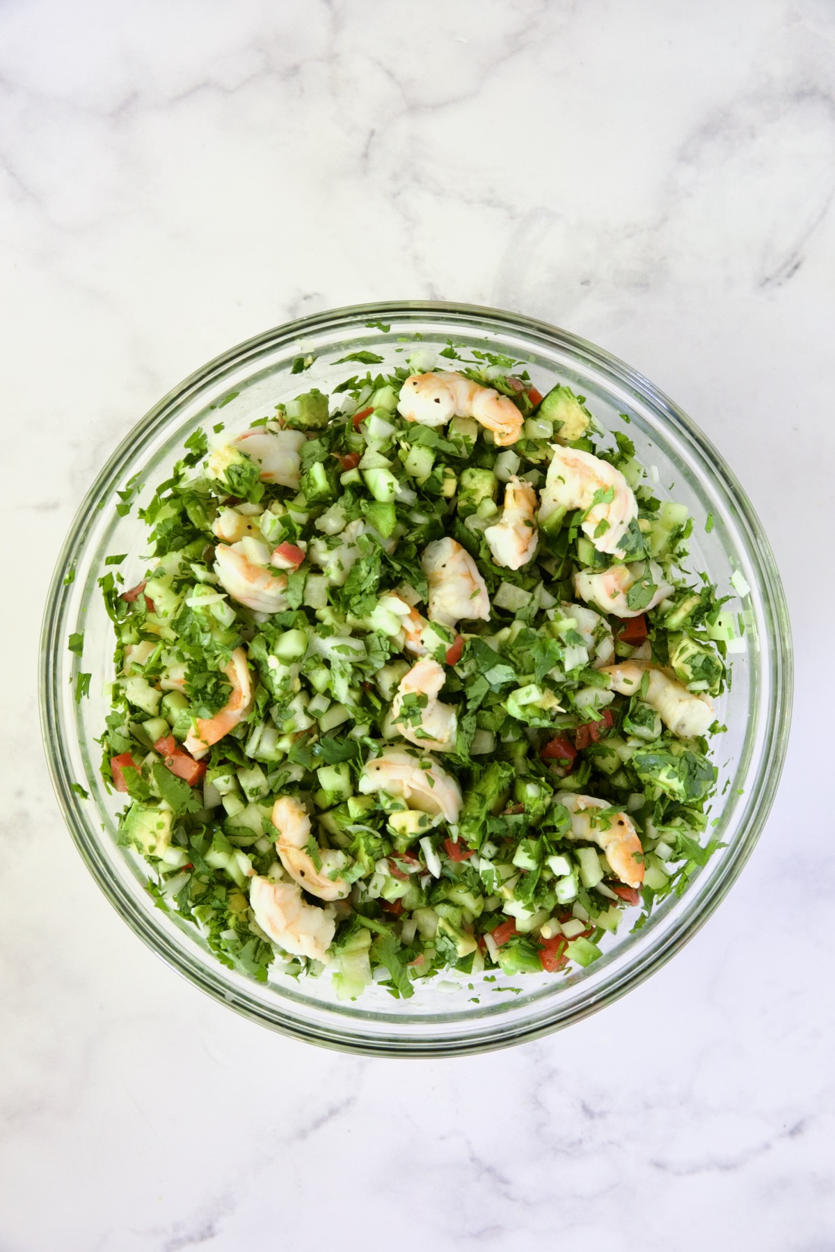 Shrimp added to vegetables in glass bowl.