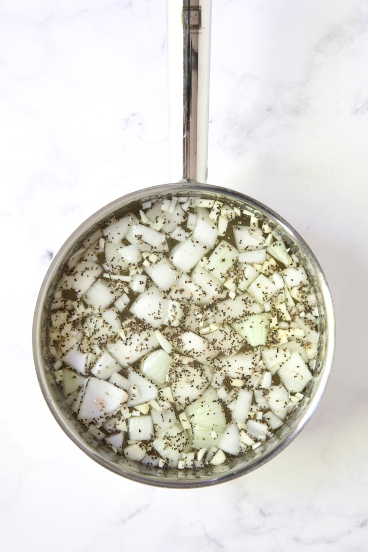 Chunks of onions, salt and pepper in stainless steel saucepan.