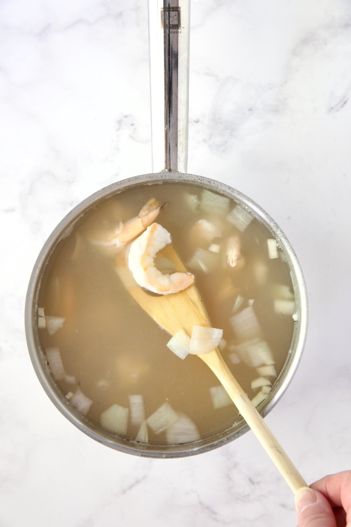 Cooked shrimp in hot water with onions in stainless steel saucepan.