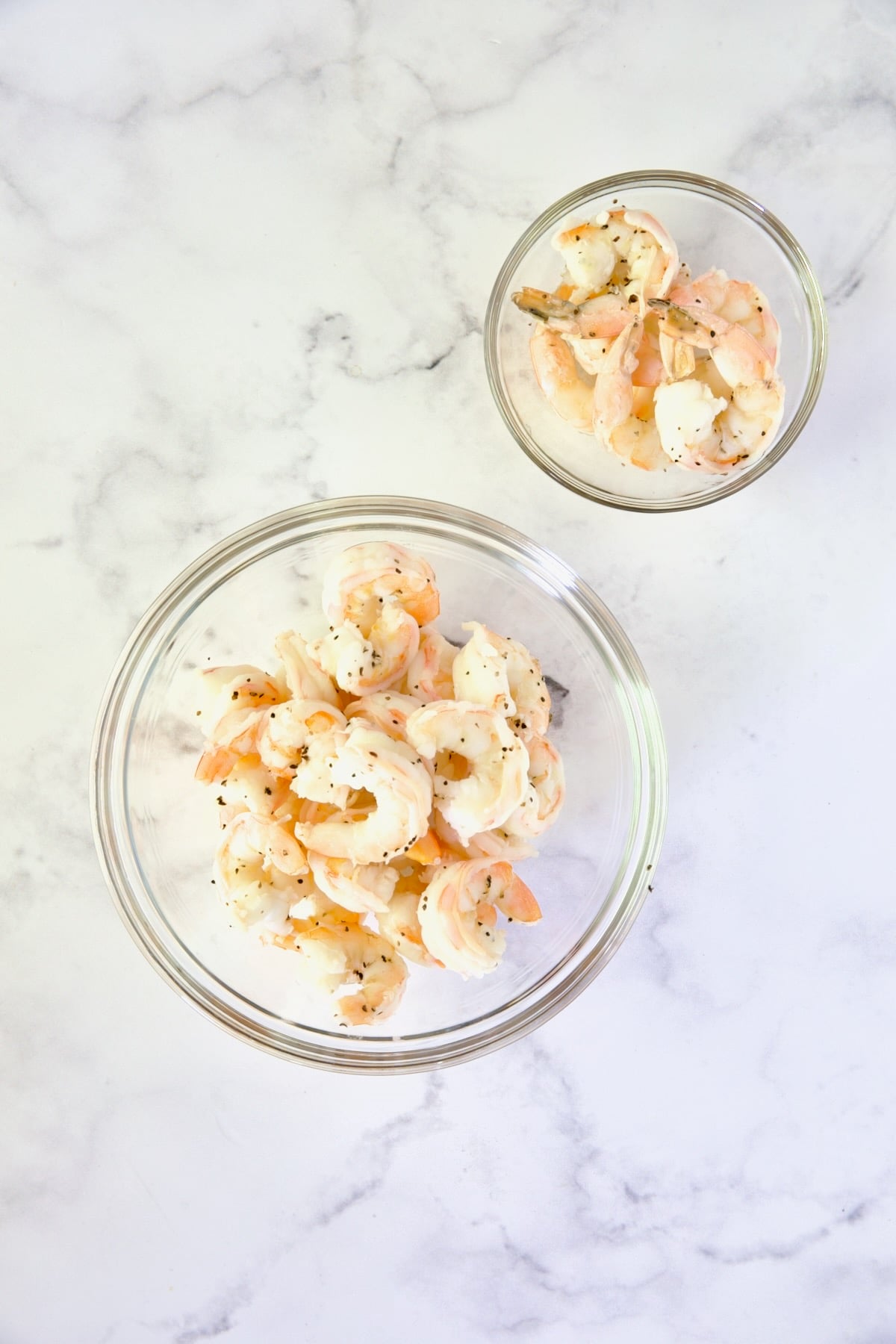 Two bowls of cooked shrimp: One with tails removed and the other with tails.