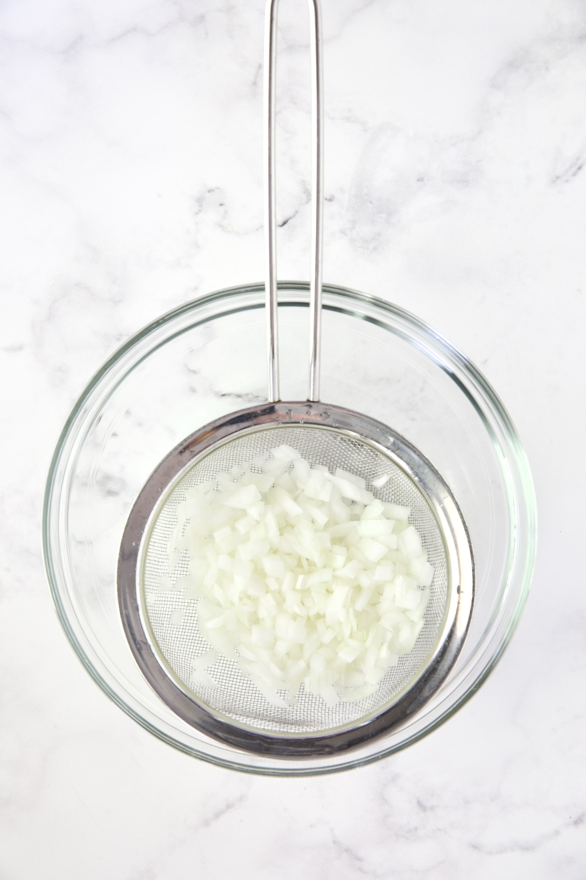 Onions in sieve set over glass bowl.
