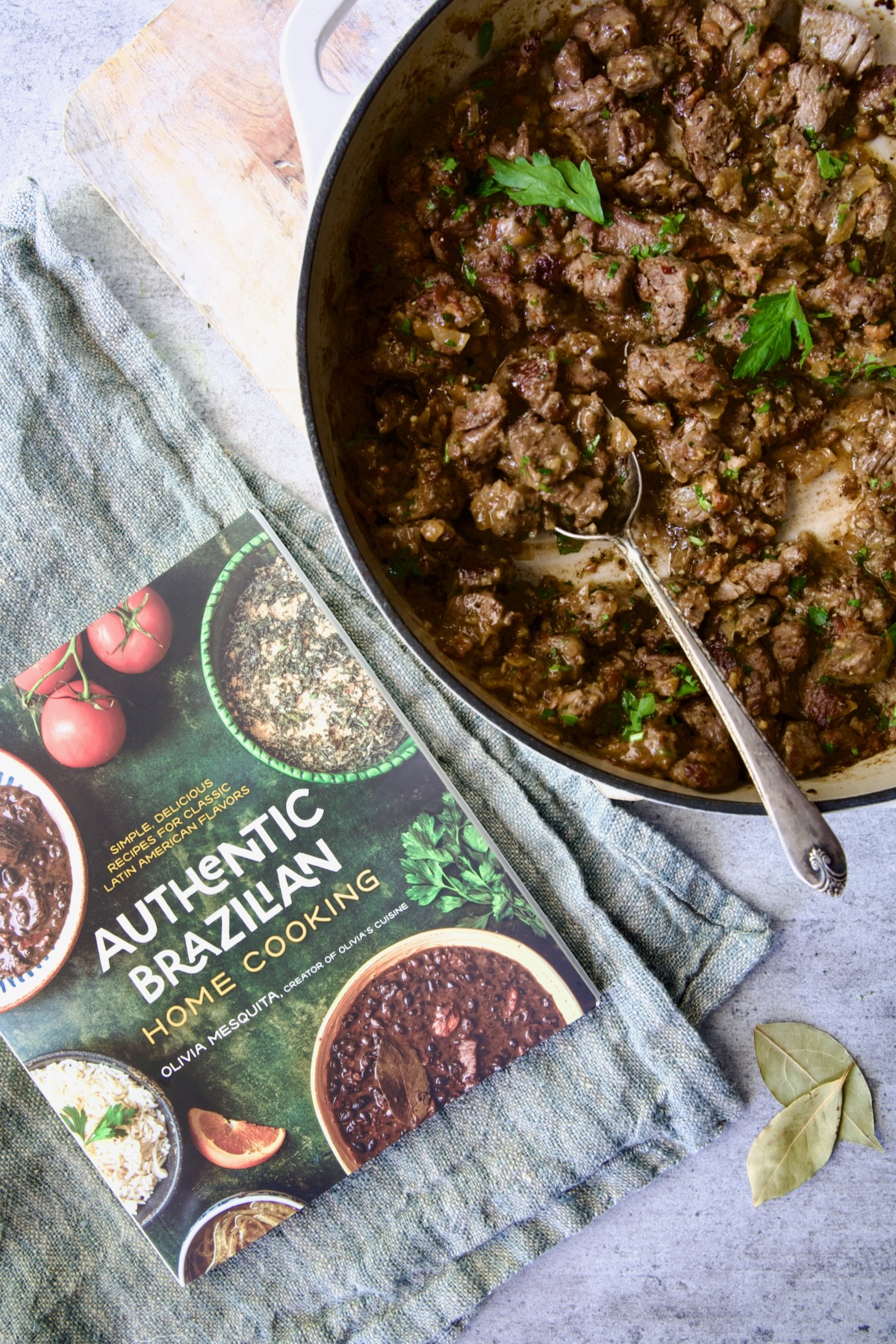 Authentic Brazilian Home Cooking cookbook with beef tips in white enamel cast iron skillet.