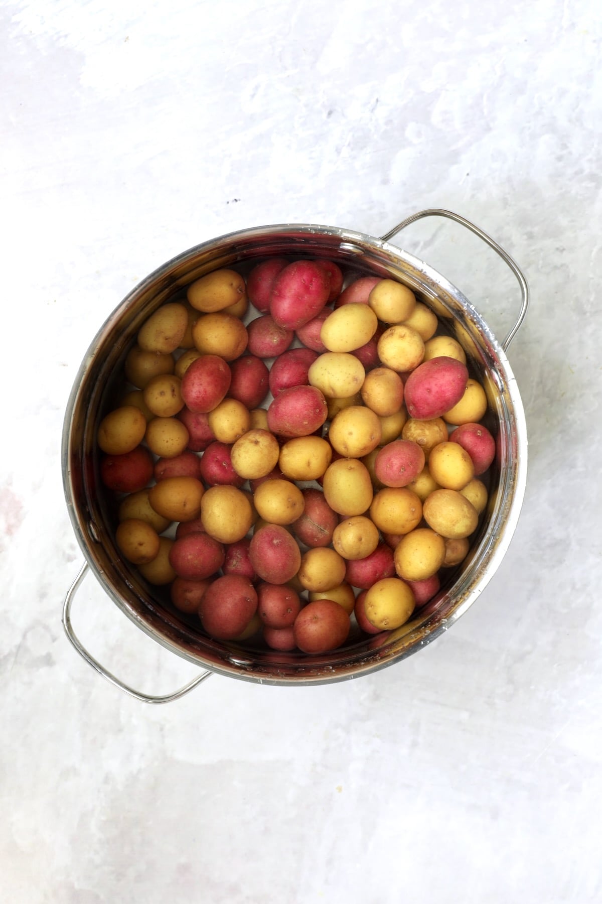 Red and yellow new potatoes in stainless steel pot about to get boiled.
