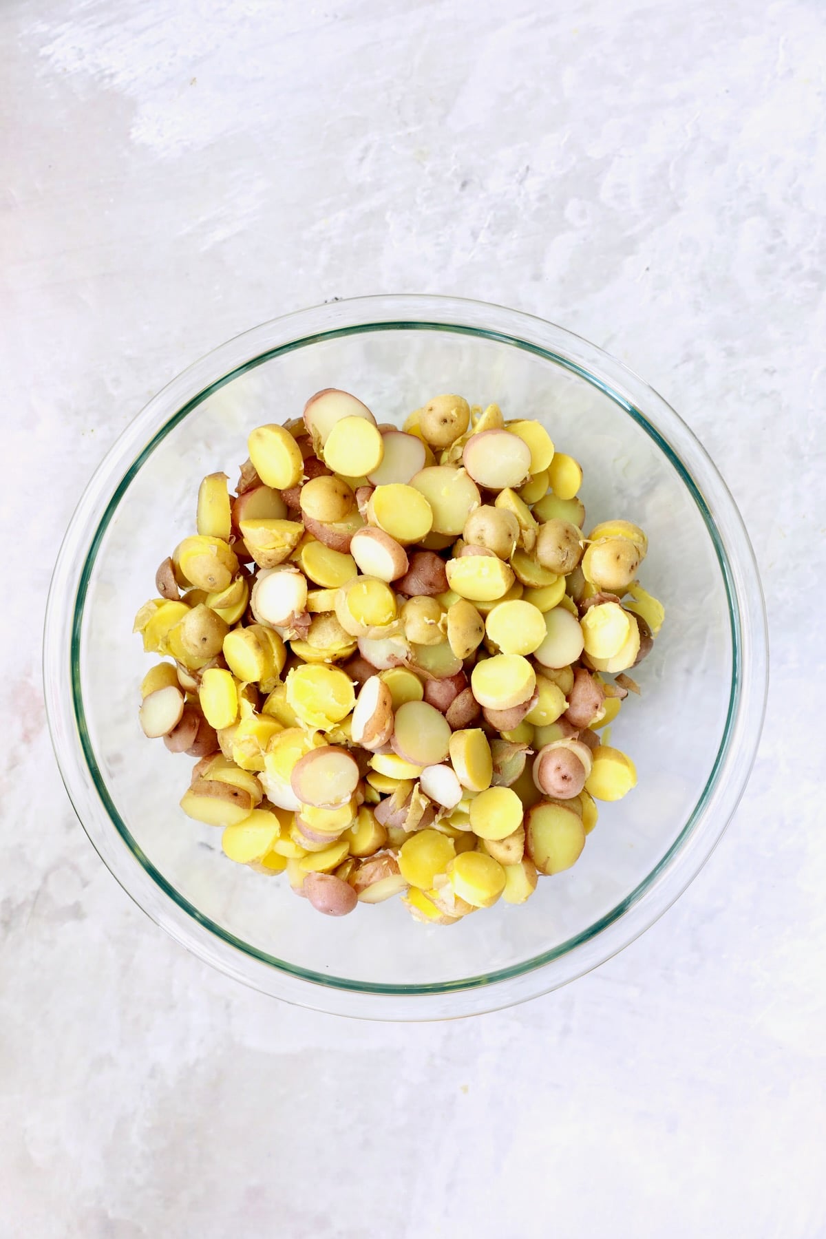 Sliced, cooked red and yellow new potatoes in glass bowl.