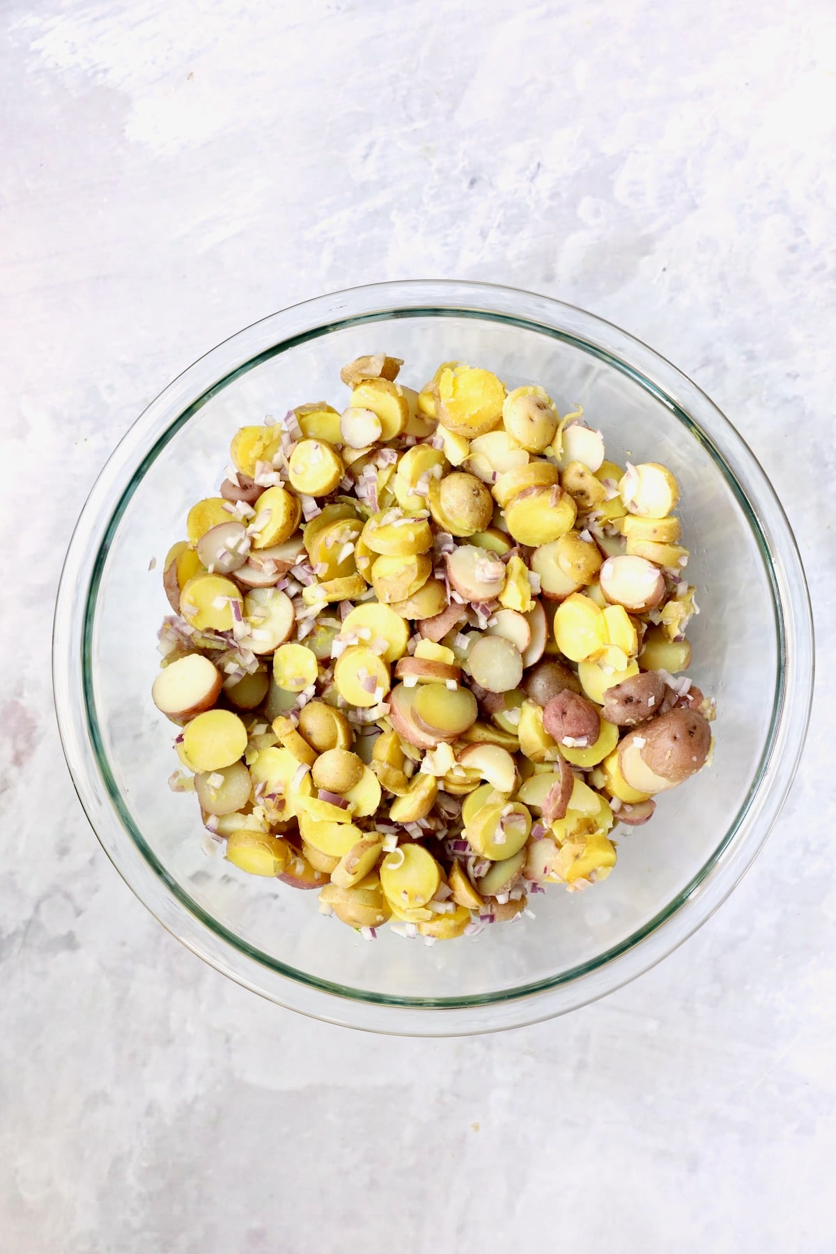Sliced, cooked red and yellow new potatoes and shallots in glass bowl.