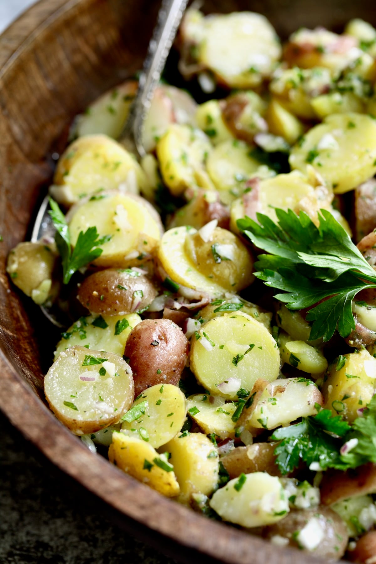 French Potato Salad in wood bowl with serving utensil garnished with fresh parsley.